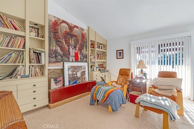 sitting room featuring built in shelves, light carpet, and lofted ceiling