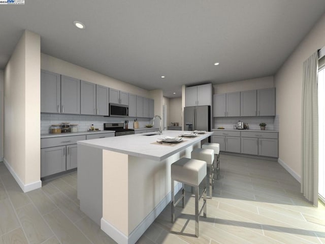 kitchen featuring sink, tasteful backsplash, a kitchen bar, a center island with sink, and appliances with stainless steel finishes