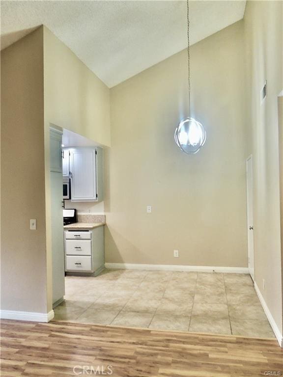 kitchen with high vaulted ceiling, light wood-type flooring, and decorative light fixtures