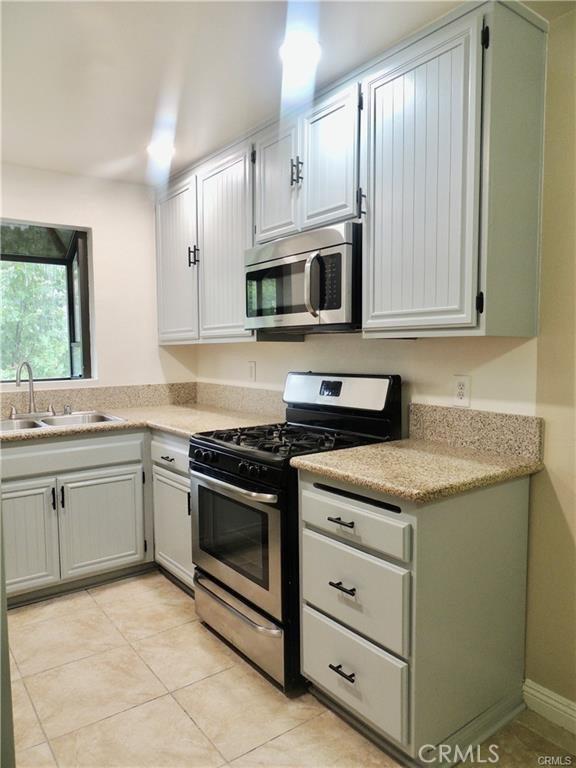 kitchen featuring light tile patterned flooring, appliances with stainless steel finishes, white cabinetry, and sink