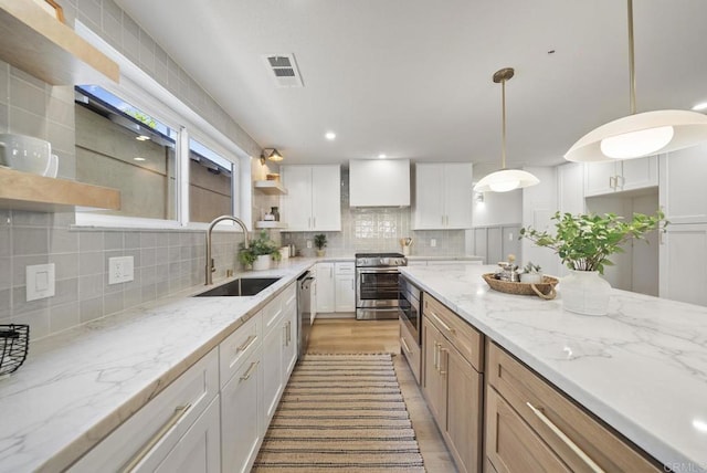 kitchen featuring sink, wall chimney exhaust hood, hanging light fixtures, stainless steel appliances, and white cabinets