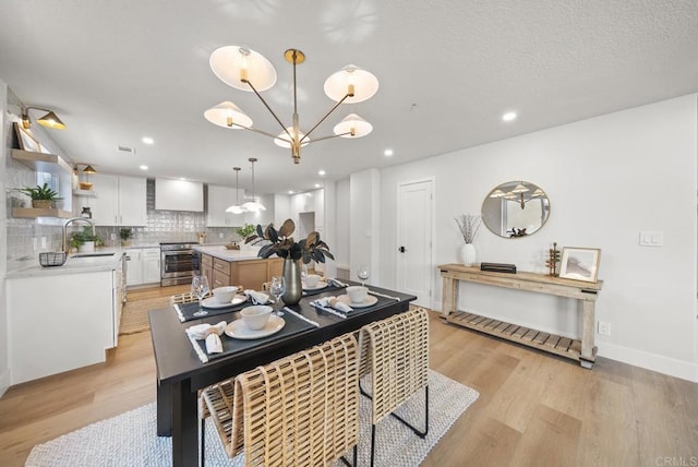 dining space with sink, light hardwood / wood-style floors, and a notable chandelier