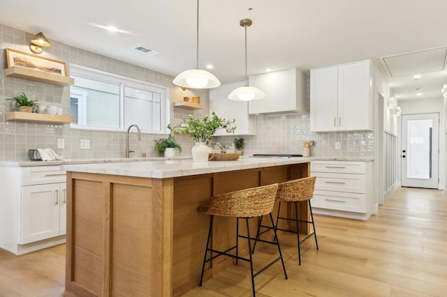 kitchen featuring a center island, wall chimney range hood, decorative light fixtures, light hardwood / wood-style floors, and white cabinetry