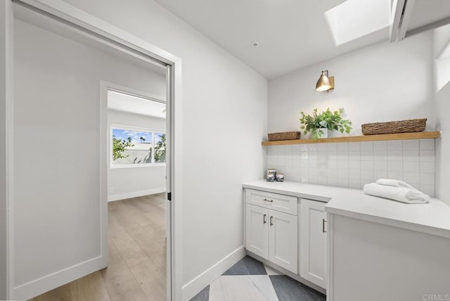 bar with tasteful backsplash, a skylight, white cabinetry, and light wood-type flooring