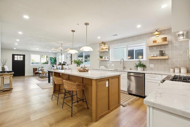 kitchen featuring light stone countertops, white cabinetry, stainless steel dishwasher, and a kitchen island