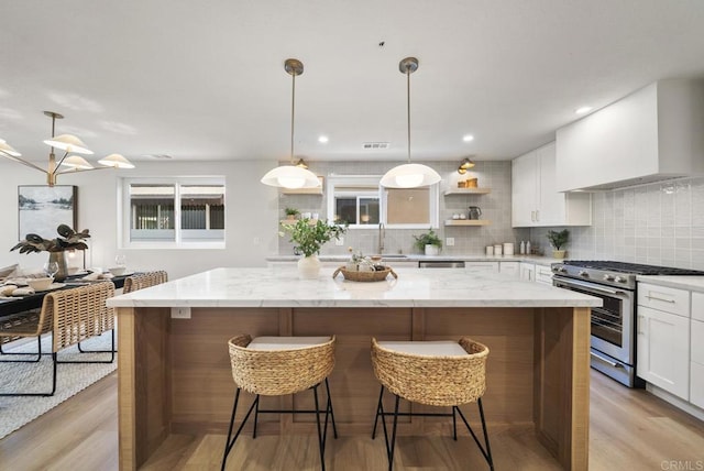 kitchen featuring white cabinets, wall chimney range hood, decorative light fixtures, light stone counters, and stainless steel appliances