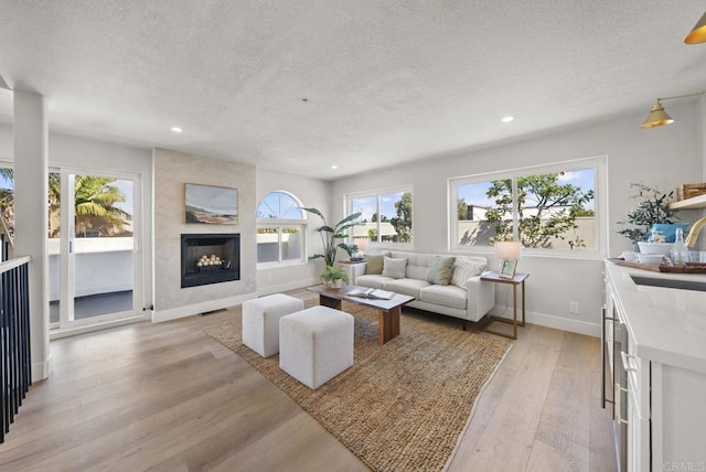 living room featuring a large fireplace, sink, a textured ceiling, and light hardwood / wood-style flooring