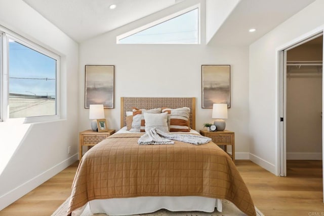 bedroom featuring a closet, light wood-type flooring, a walk in closet, and vaulted ceiling