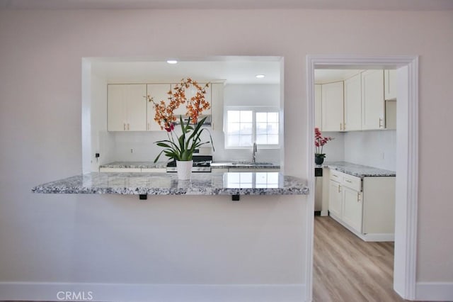 kitchen with sink, white cabinetry, light hardwood / wood-style floors, kitchen peninsula, and light stone countertops