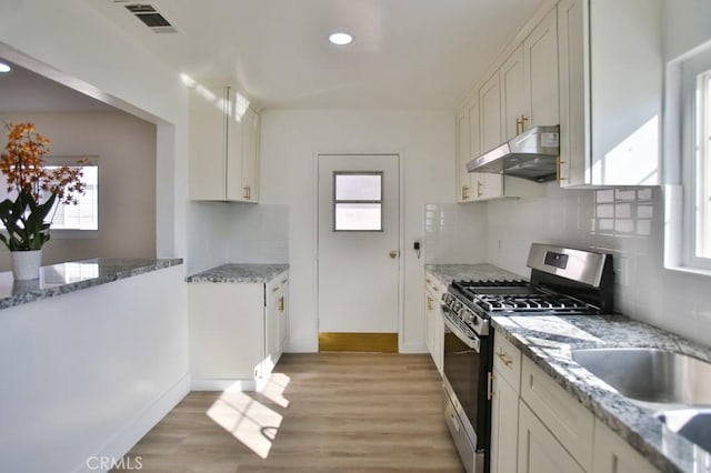 kitchen with light stone countertops, stainless steel gas range oven, light wood-type flooring, backsplash, and white cabinets