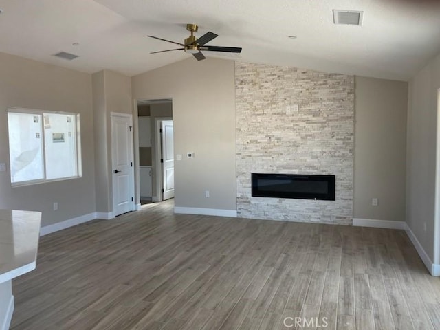 unfurnished living room with lofted ceiling, ceiling fan, a stone fireplace, and hardwood / wood-style flooring