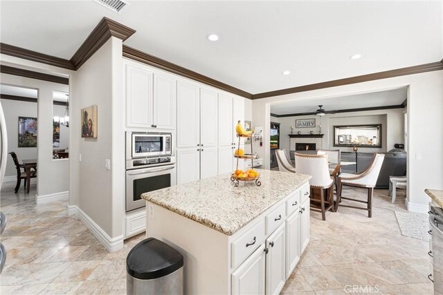 kitchen with light stone countertops, stainless steel appliances, a kitchen island, white cabinets, and ceiling fan