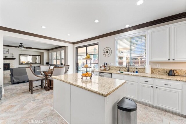 kitchen with light stone counters, crown molding, white cabinetry, ceiling fan, and sink