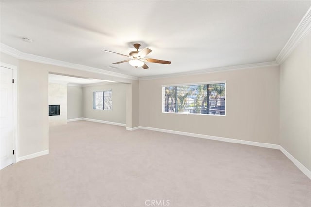 carpeted empty room featuring a fireplace, ceiling fan, and crown molding