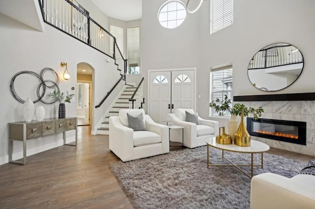 living room featuring a high ceiling, a fireplace, wood-type flooring, and a healthy amount of sunlight