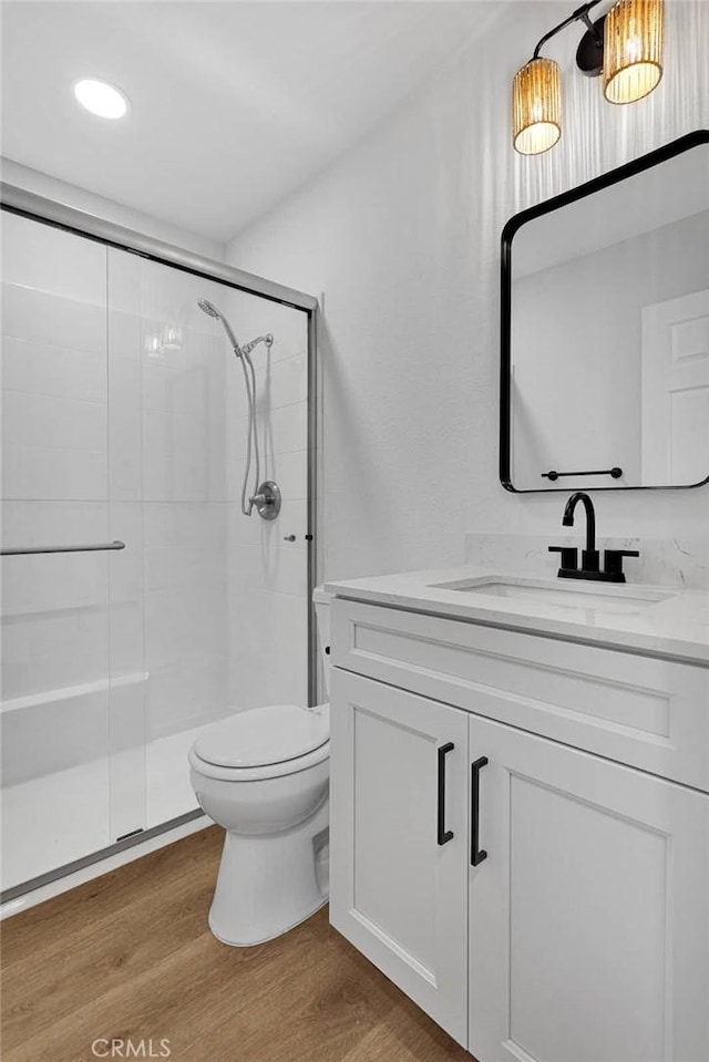 bathroom featuring toilet, wood-type flooring, vanity, and a shower with door