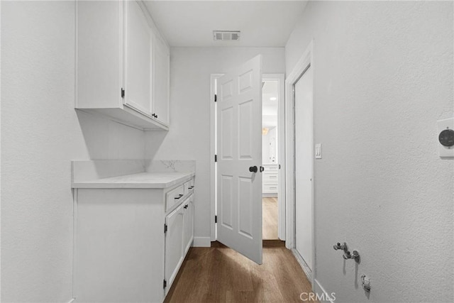 clothes washing area featuring dark hardwood / wood-style flooring and cabinets