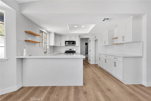 kitchen with kitchen peninsula, stainless steel appliances, light wood-type flooring, white cabinetry, and sink