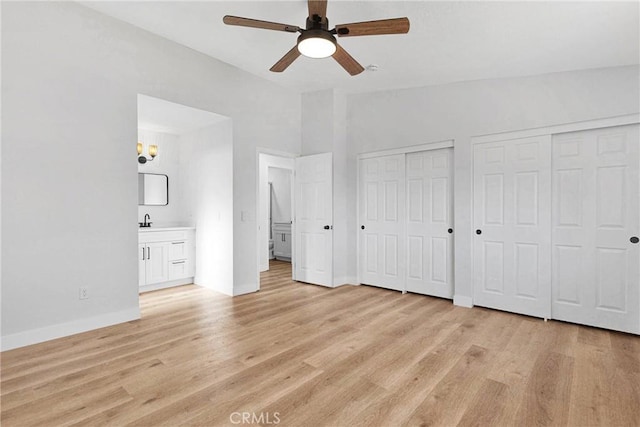 unfurnished bedroom featuring two closets, connected bathroom, ceiling fan, and light wood-type flooring