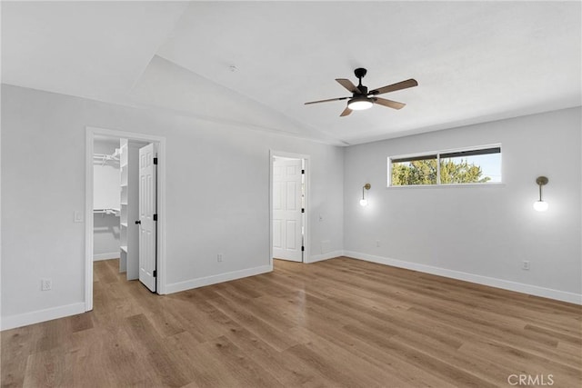 unfurnished bedroom featuring vaulted ceiling, light hardwood / wood-style flooring, a closet, a walk in closet, and ceiling fan