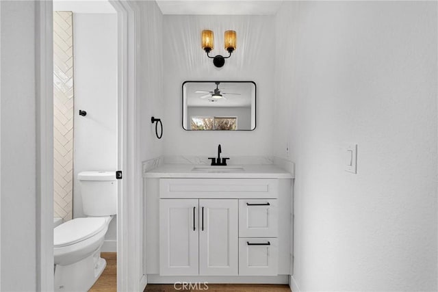 bathroom with toilet, hardwood / wood-style flooring, ceiling fan, and vanity