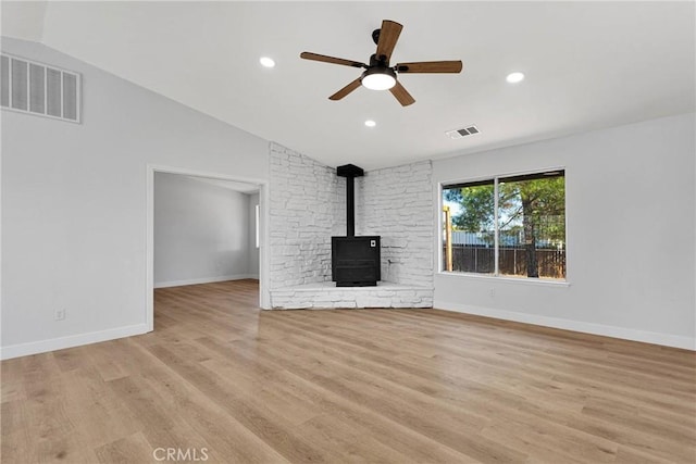 unfurnished living room with lofted ceiling, ceiling fan, a wood stove, and light wood-type flooring