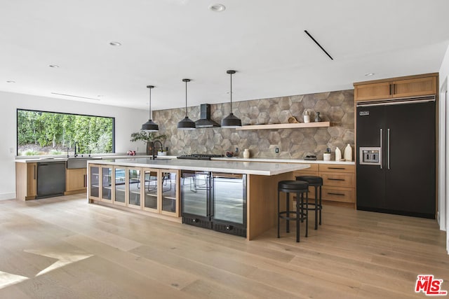 interior space featuring dishwasher, built in refrigerator, a kitchen island with sink, and wall chimney range hood