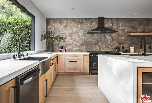 kitchen featuring dishwasher, high end black range, sink, wall chimney exhaust hood, and tasteful backsplash