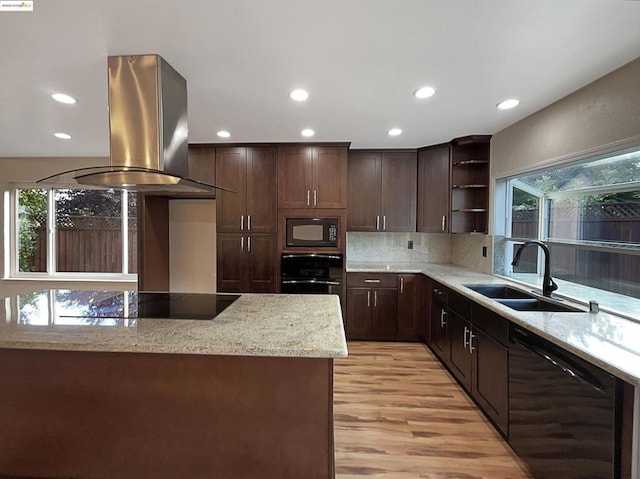 kitchen featuring light stone countertops, island exhaust hood, sink, black appliances, and light hardwood / wood-style floors