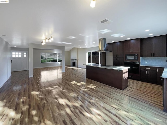 kitchen with black appliances, hardwood / wood-style flooring, a kitchen island, dark brown cabinetry, and island exhaust hood