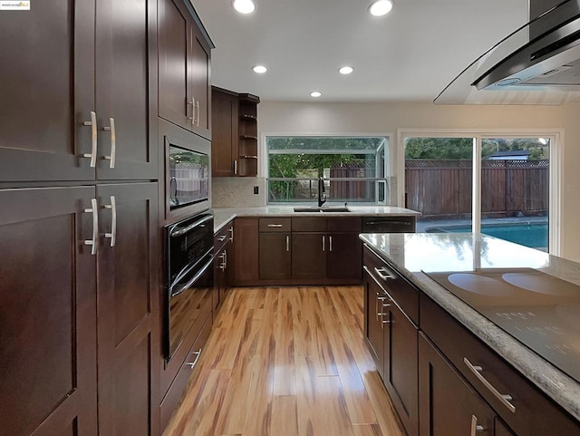 kitchen with built in microwave, wall chimney range hood, electric stovetop, sink, and light hardwood / wood-style flooring