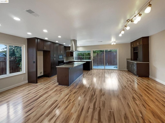 kitchen with island exhaust hood, light wood-type flooring, dark brown cabinetry, black microwave, and a kitchen island