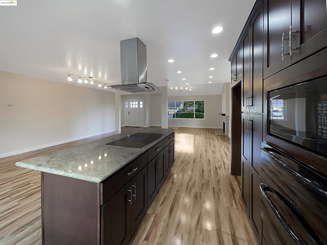 kitchen with light stone counters, light hardwood / wood-style flooring, island range hood, a kitchen island, and black appliances