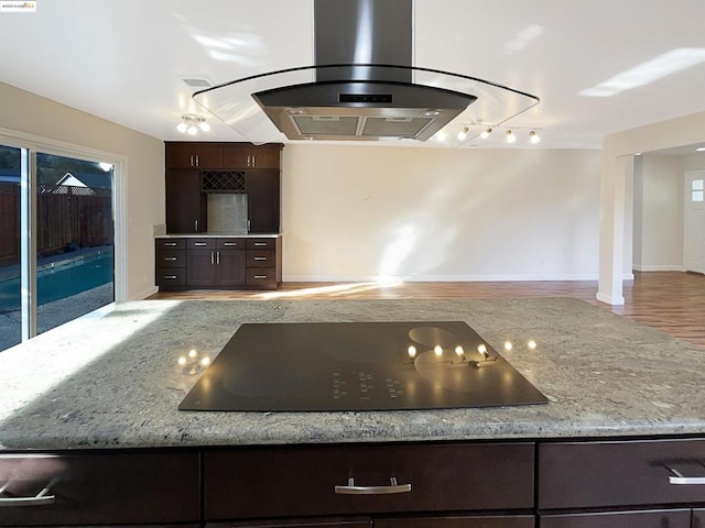 kitchen with island exhaust hood, dark brown cabinetry, black electric cooktop, and light stone counters