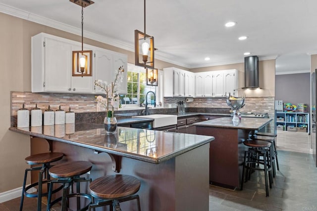 kitchen with kitchen peninsula, wall chimney exhaust hood, decorative light fixtures, white cabinetry, and sink