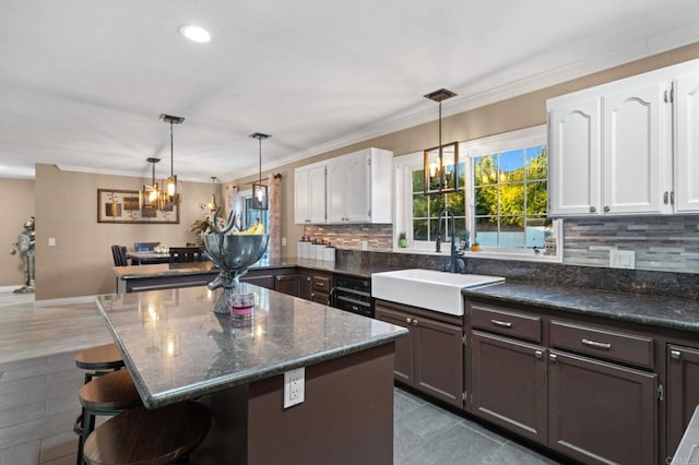 kitchen with pendant lighting, a kitchen bar, white cabinets, dark stone counters, and sink