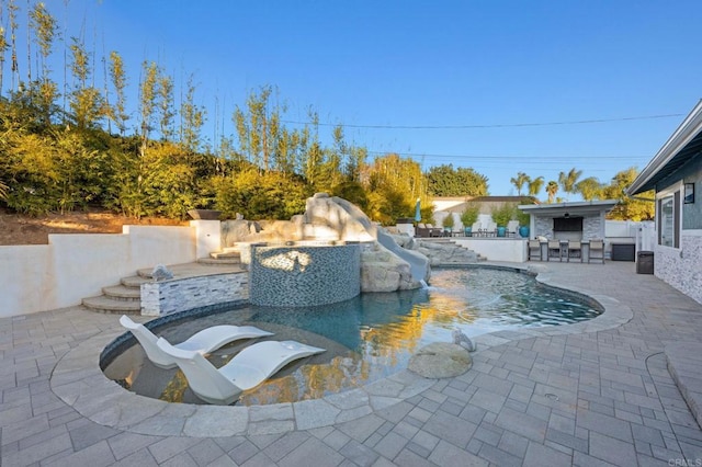 view of swimming pool with an outdoor bar, a water slide, exterior kitchen, and a patio