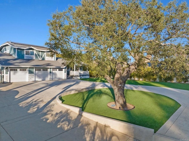 view of front facade featuring stone siding, a garage, concrete driveway, and a front yard