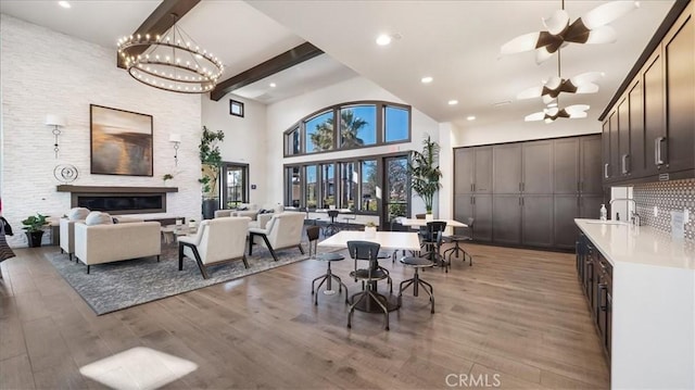 dining area with sink, a towering ceiling, a large fireplace, light hardwood / wood-style floors, and beamed ceiling