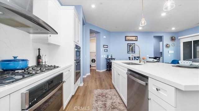 kitchen featuring hanging light fixtures, sink, white cabinets, wall chimney range hood, and stainless steel appliances