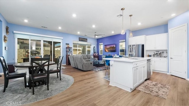 kitchen with white cabinetry, a kitchen island with sink, light hardwood / wood-style flooring, pendant lighting, and stainless steel fridge