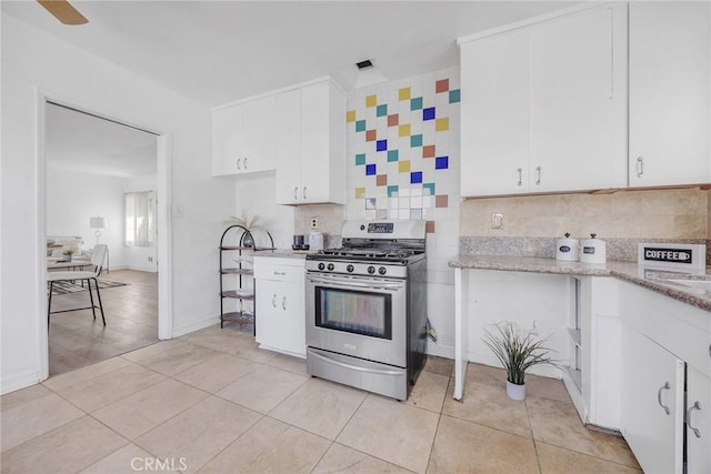 kitchen featuring stainless steel gas range, light tile patterned floors, ceiling fan, white cabinets, and backsplash