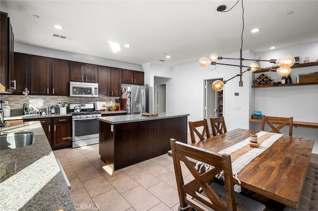 kitchen with light stone countertops, appliances with stainless steel finishes, tasteful backsplash, an inviting chandelier, and sink