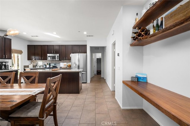 kitchen with light tile patterned floors, backsplash, dark brown cabinets, and stainless steel appliances