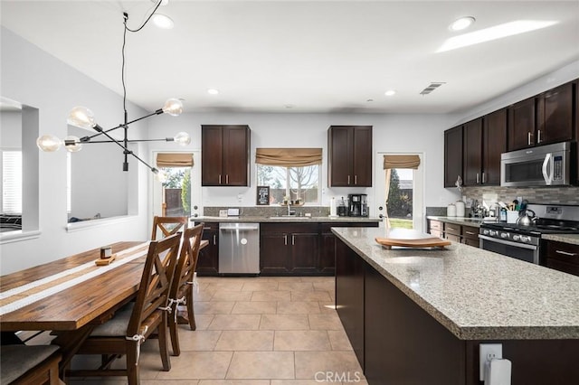 kitchen with dark brown cabinetry, a kitchen island, stainless steel appliances, tasteful backsplash, and a chandelier