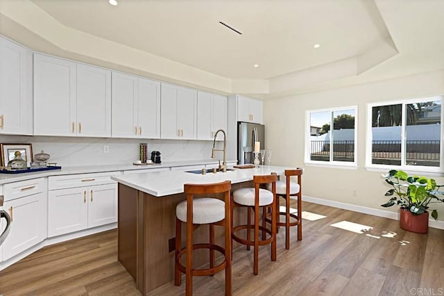 kitchen with stainless steel refrigerator with ice dispenser, a kitchen breakfast bar, a center island with sink, white cabinets, and light hardwood / wood-style floors