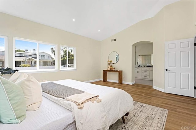 bedroom with light hardwood / wood-style floors, ensuite bath, and lofted ceiling