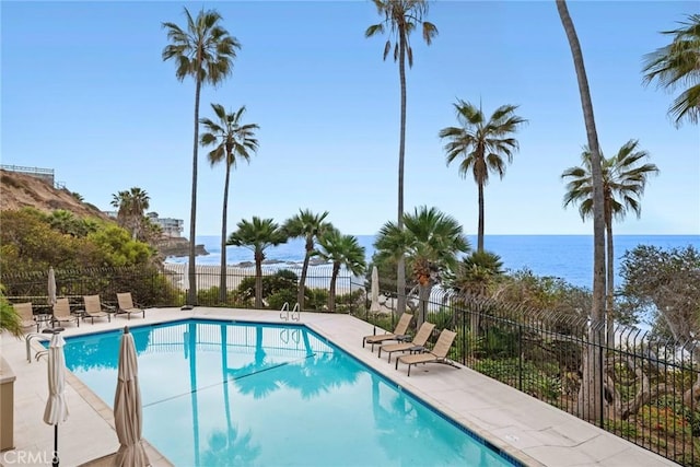 community pool with a patio area, a water view, and fence