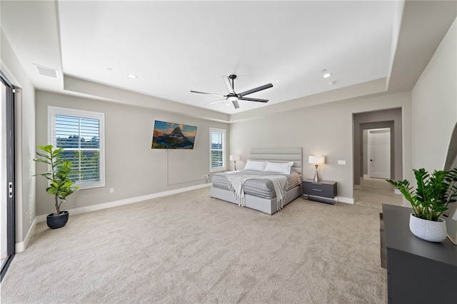 bedroom featuring multiple windows, light colored carpet, ceiling fan, and a tray ceiling