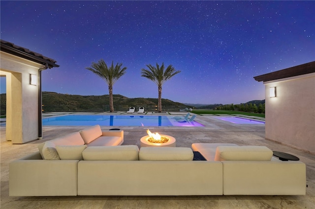 pool at dusk featuring a mountain view, an outdoor fire pit, and a patio area